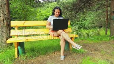 在公园里坐长凳的年轻女人用笔记本电脑工作。